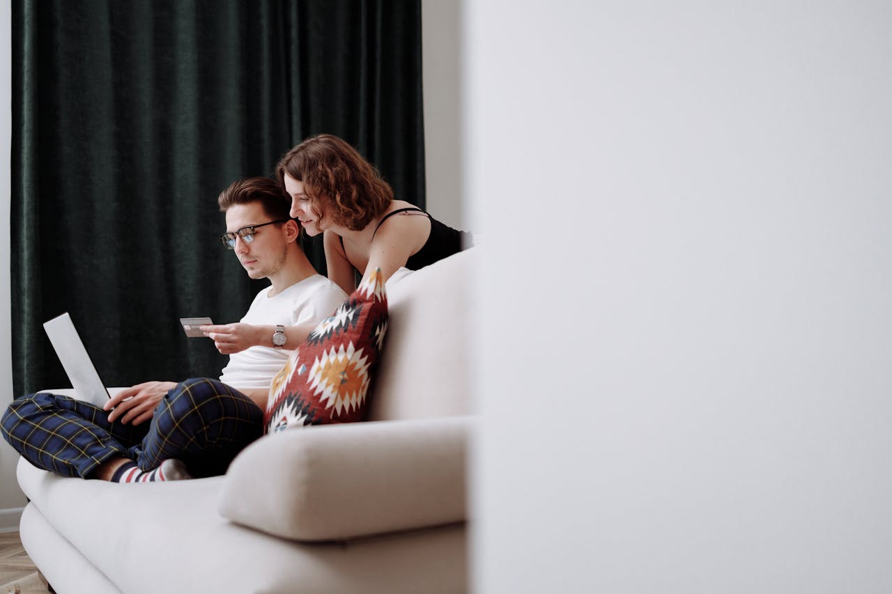 A couple sits comfortably on the couch while shopping online together.